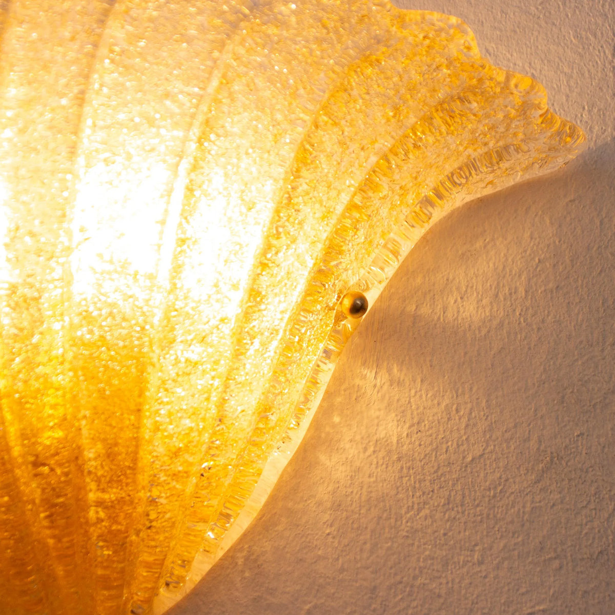 Close-up of the lit amber Murano glass shell sconce and its brass mounting screw