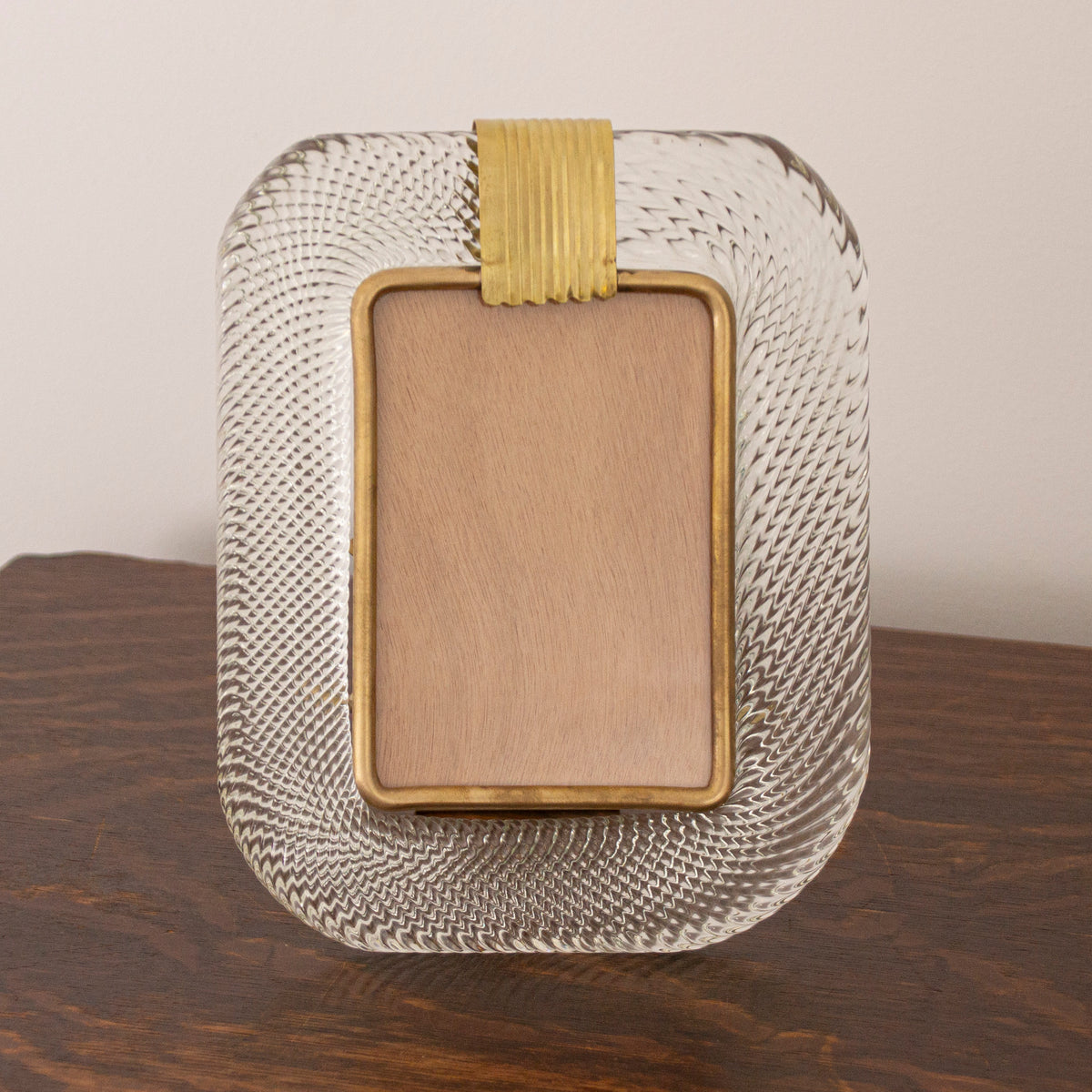 Front view of the clear Murano glass picture frame with brass band on a wooden table