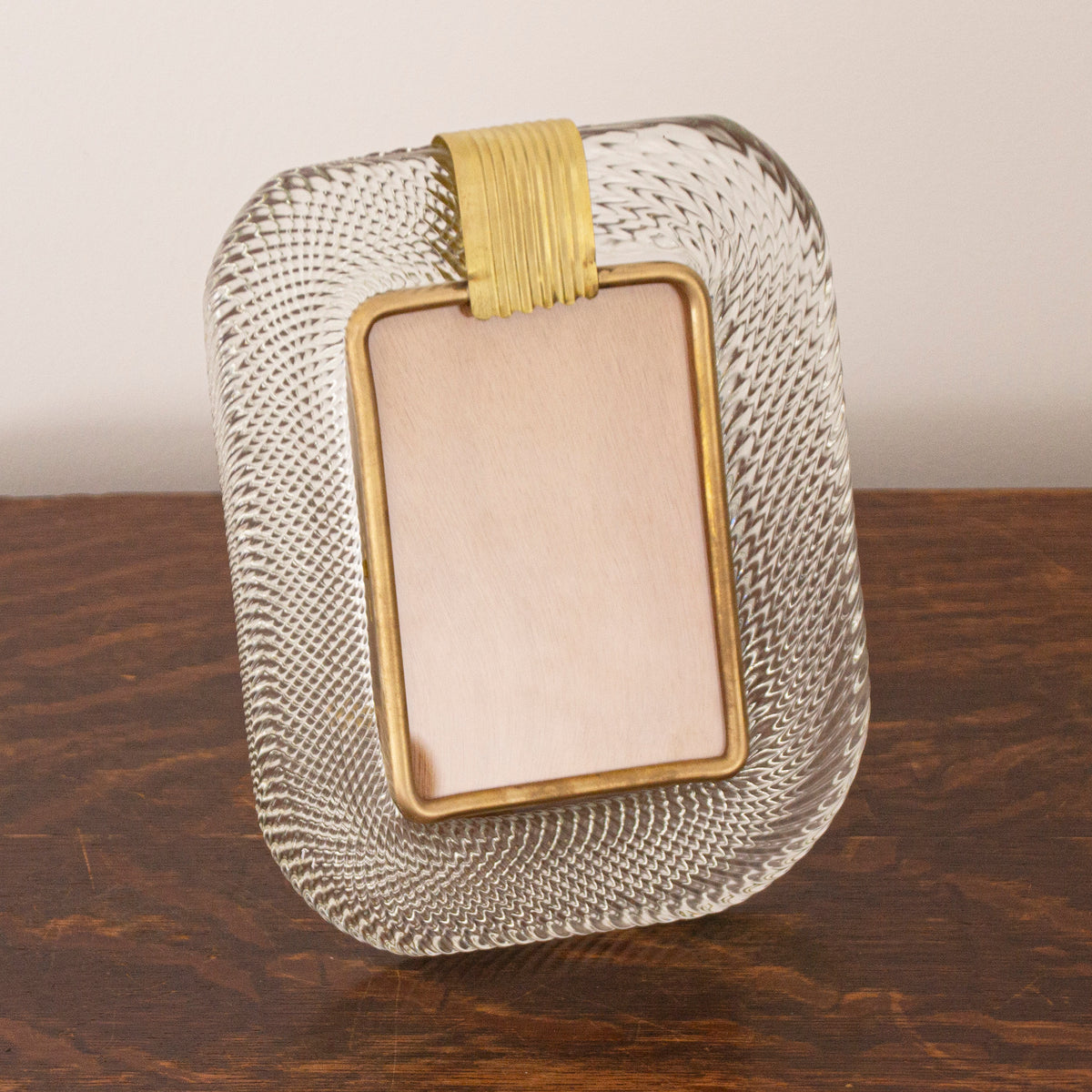 Clear Murano glass picture frame with brass details on a dark wooden table