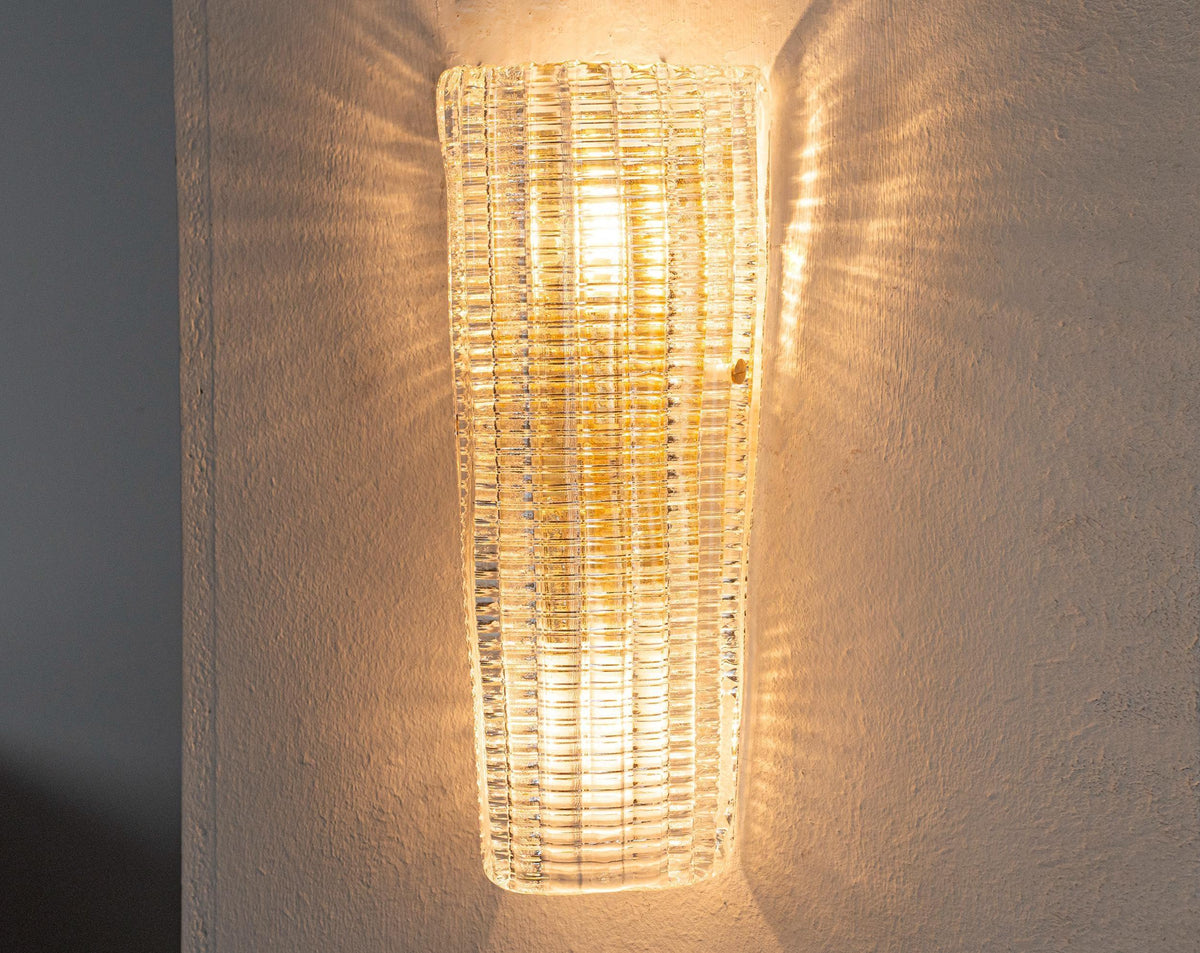 Clear textured Murano glass wall sconce, lit, casting light patterns on the wall