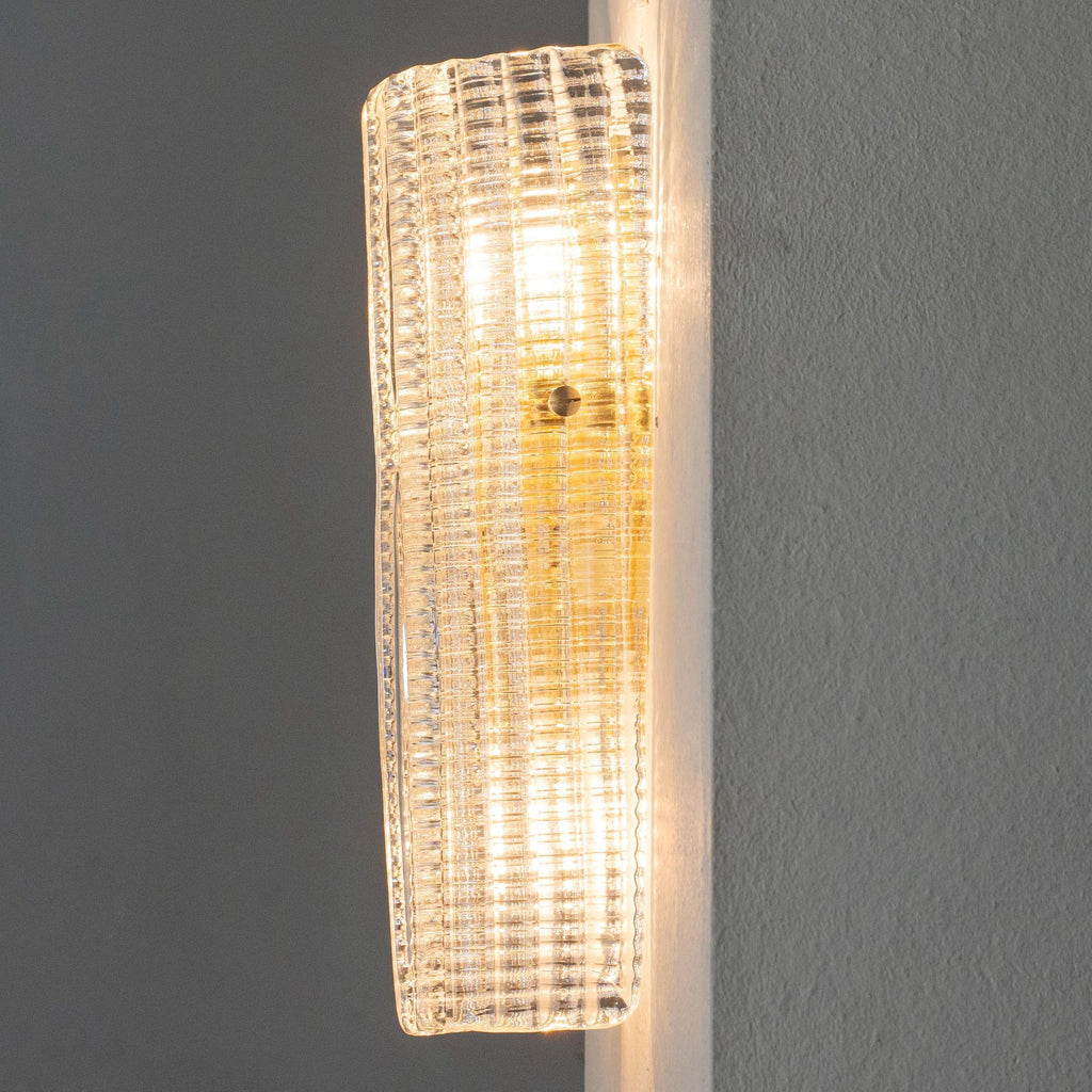 Clear textured Murano glass wall sconce, lit, side view on a grey wall