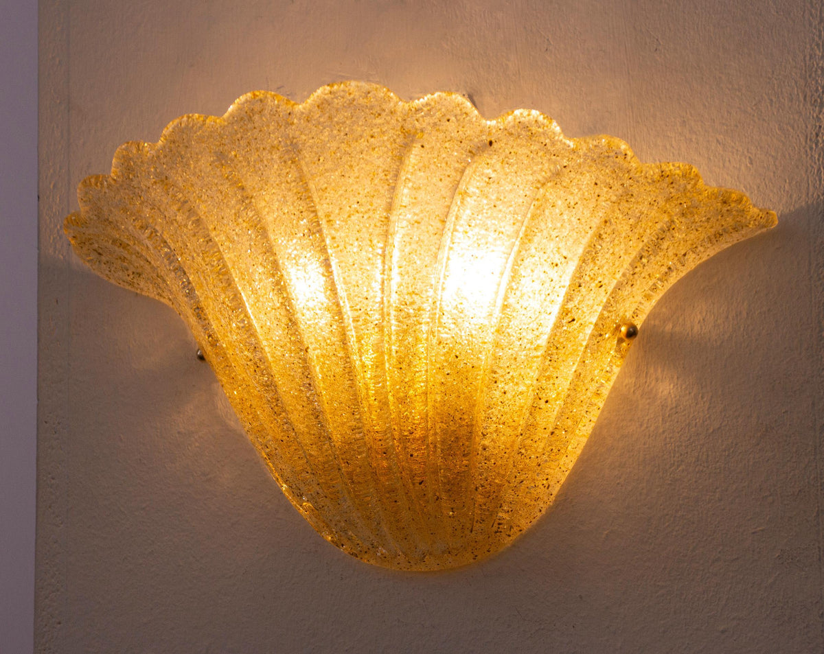 Gold Murano glass shell wall sconce, lit, angled view with warm amber glow