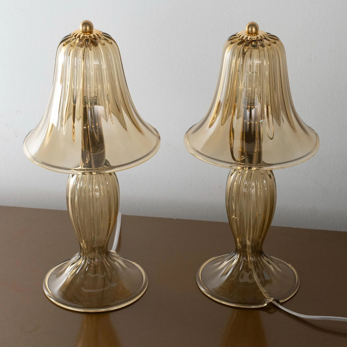 Front view of two smoky Murano glass table lamps with ribbed shades and gold finials